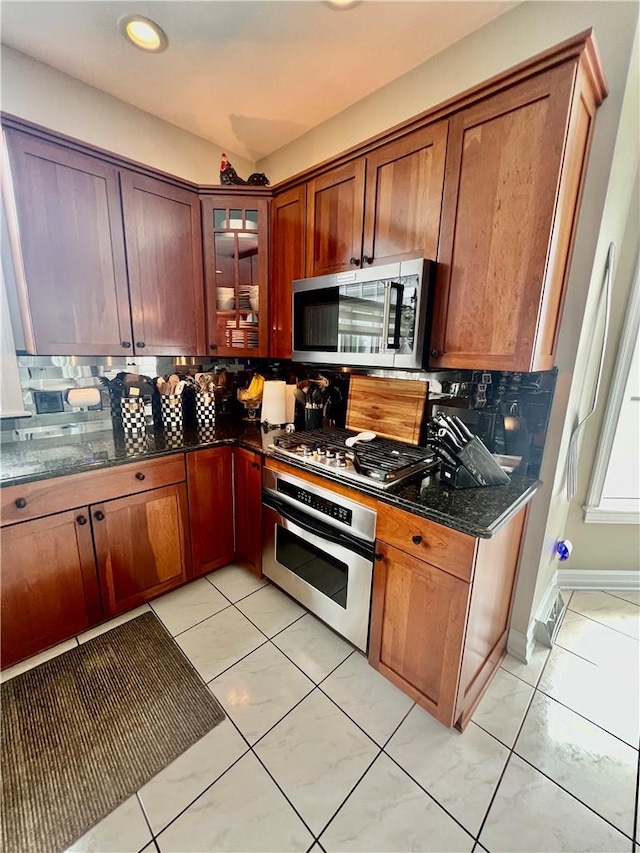 kitchen with light tile patterned floors, backsplash, stainless steel appliances, and dark stone countertops