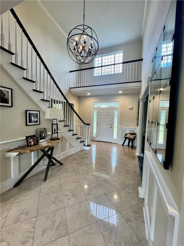 foyer entrance with a high ceiling, an inviting chandelier, a wealth of natural light, and ornamental molding