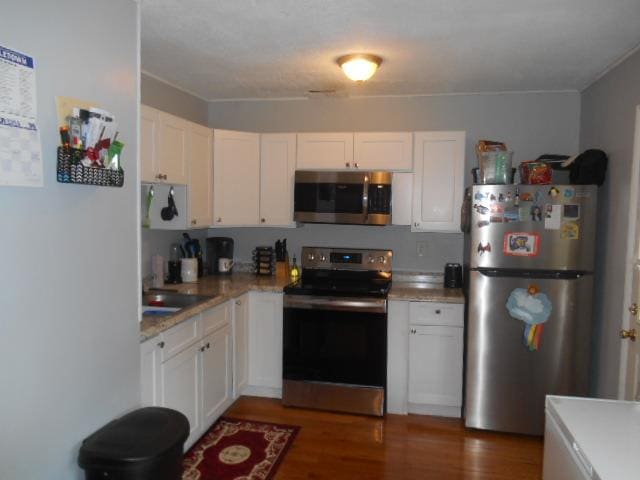 kitchen with appliances with stainless steel finishes, light stone counters, dark wood-type flooring, sink, and white cabinets