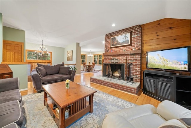 living room with vaulted ceiling, light wood-type flooring, a fireplace, and an inviting chandelier