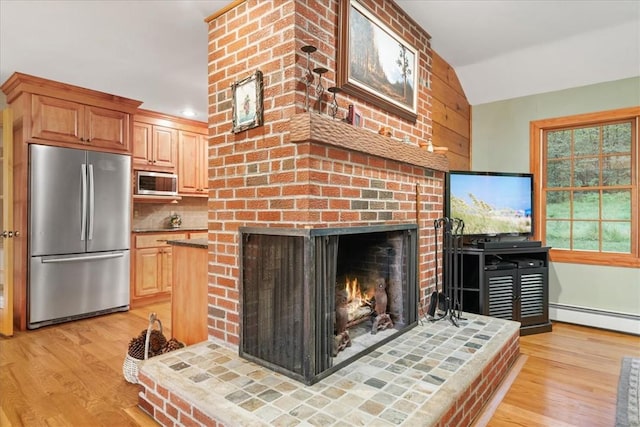 living room featuring baseboard heating, a brick fireplace, lofted ceiling, and light wood-type flooring