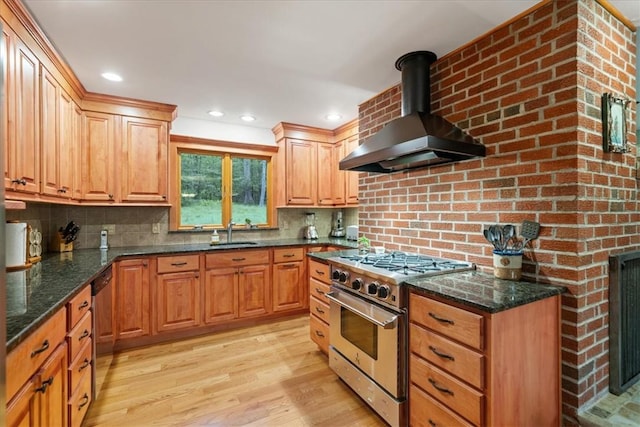 kitchen featuring wall chimney range hood, sink, dark stone countertops, appliances with stainless steel finishes, and light hardwood / wood-style floors