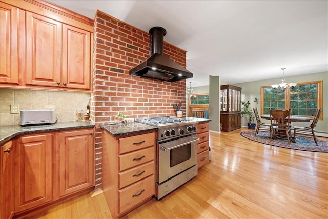 kitchen with light wood-type flooring, wall chimney exhaust hood, high end stainless steel range oven, decorative light fixtures, and an inviting chandelier