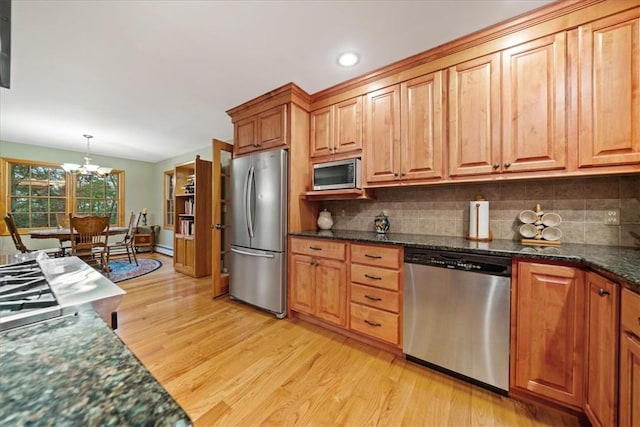 kitchen with backsplash, hanging light fixtures, light hardwood / wood-style floors, stainless steel appliances, and a chandelier