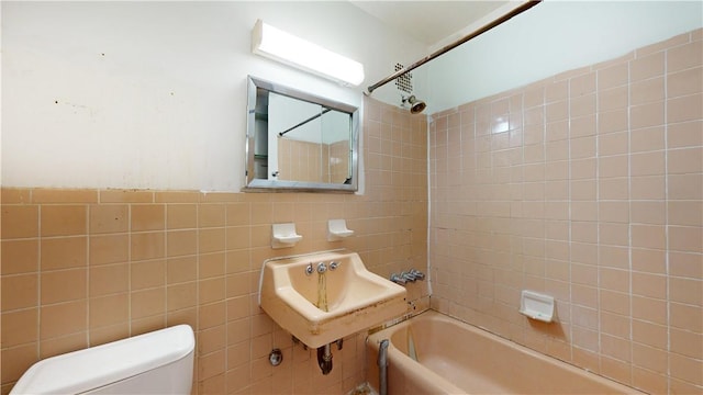 bathroom with tiled shower / bath combo, tile walls, and toilet