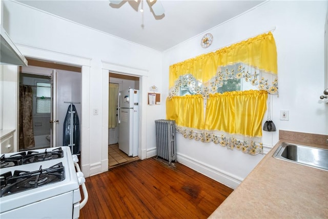 kitchen featuring radiator, white appliances, ceiling fan, dark wood-type flooring, and wall chimney range hood