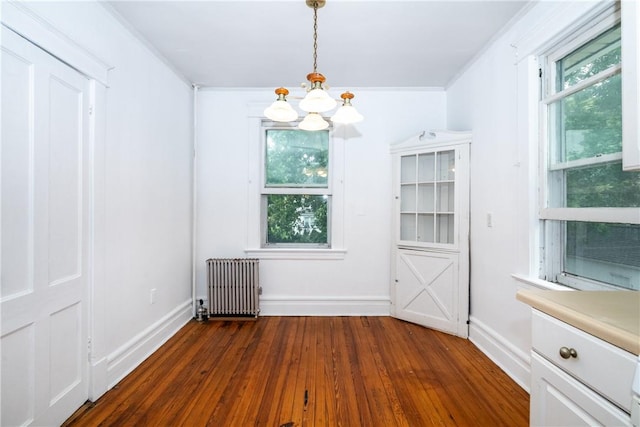 unfurnished dining area featuring radiator heating unit, dark hardwood / wood-style floors, an inviting chandelier, and crown molding