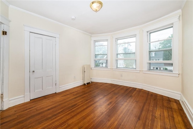 spare room featuring dark wood-type flooring, crown molding, radiator heating unit, and a healthy amount of sunlight