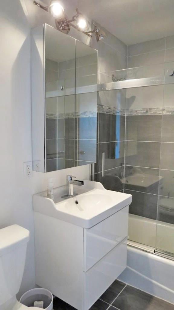 full bathroom featuring tile patterned flooring, toilet, vanity, and combined bath / shower with glass door