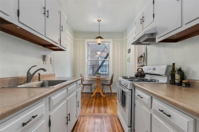 kitchen with white cabinetry, white gas stove, sink, hanging light fixtures, and light hardwood / wood-style flooring