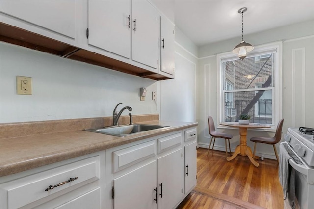 kitchen featuring pendant lighting, sink, stainless steel range, light hardwood / wood-style floors, and white cabinetry