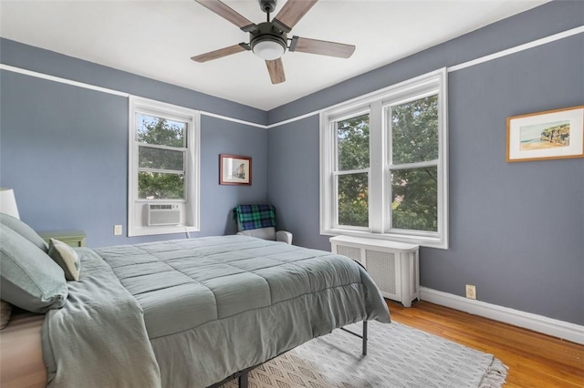 bedroom featuring multiple windows, radiator heating unit, light hardwood / wood-style flooring, and ceiling fan