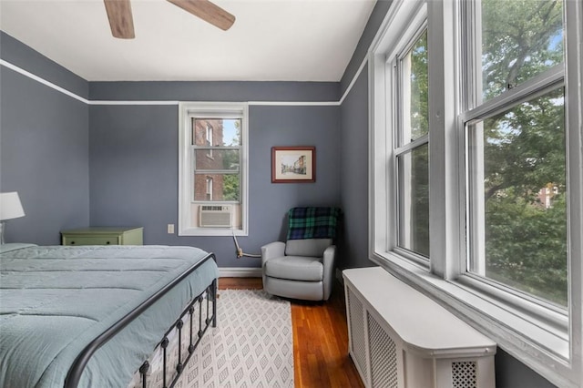 bedroom with multiple windows, ceiling fan, radiator heating unit, and dark hardwood / wood-style floors