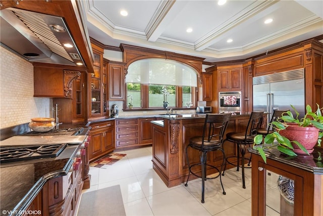 kitchen with wall chimney exhaust hood, ornamental molding, dark stone countertops, a kitchen island, and appliances with stainless steel finishes