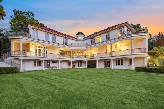 back house at dusk featuring a yard and a balcony