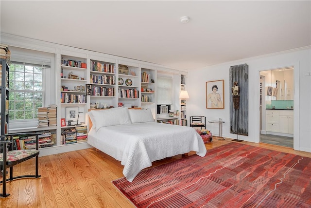 bedroom with light wood-type flooring, crown molding, and connected bathroom