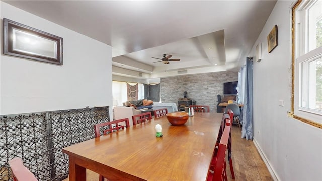 dining area with wood-type flooring, a tray ceiling, a wood stove, and plenty of natural light