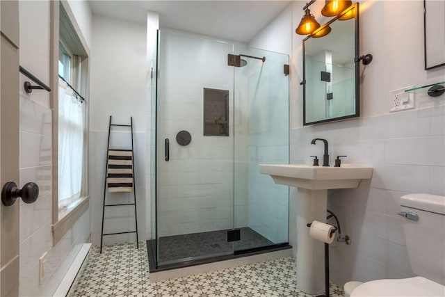 bathroom with a shower with door, toilet, tile walls, and a healthy amount of sunlight