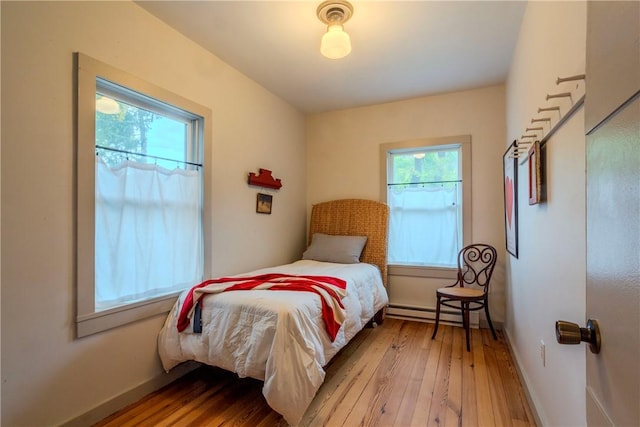 bedroom featuring baseboard heating, multiple windows, and wood-type flooring