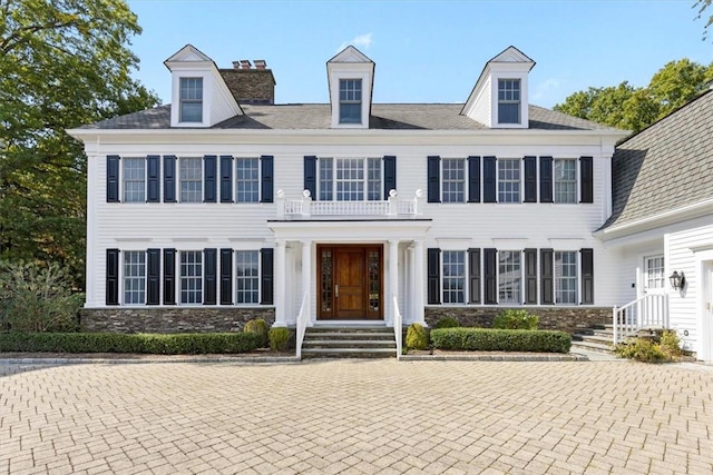 colonial house with stone siding, a chimney, and a balcony