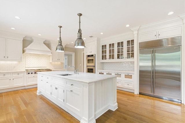 kitchen with white cabinets, premium range hood, stainless steel appliances, and a sink