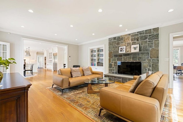 living area with built in shelves, crown molding, a fireplace, recessed lighting, and light wood-style flooring