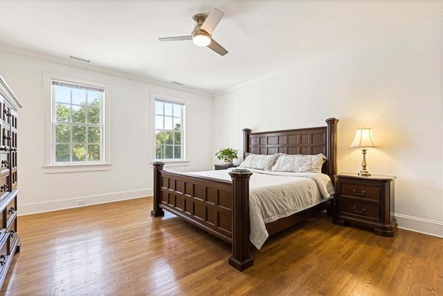 bedroom with ornamental molding, visible vents, baseboards, and wood finished floors