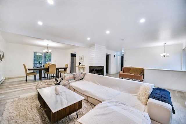 living room featuring a notable chandelier, a large fireplace, and light wood-type flooring