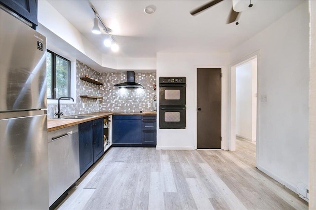 kitchen with wall chimney range hood, sink, decorative backsplash, appliances with stainless steel finishes, and butcher block counters