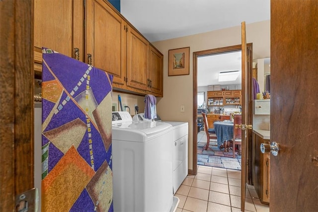 clothes washing area featuring light tile patterned floors, washer and clothes dryer, and cabinets