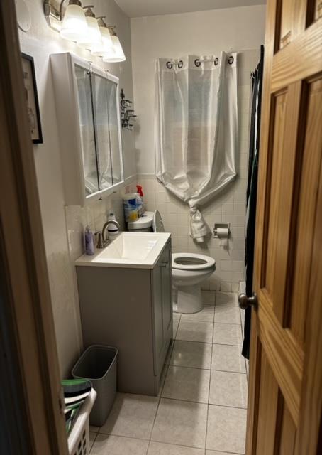 bathroom featuring toilet, vanity, tile patterned floors, and tile walls