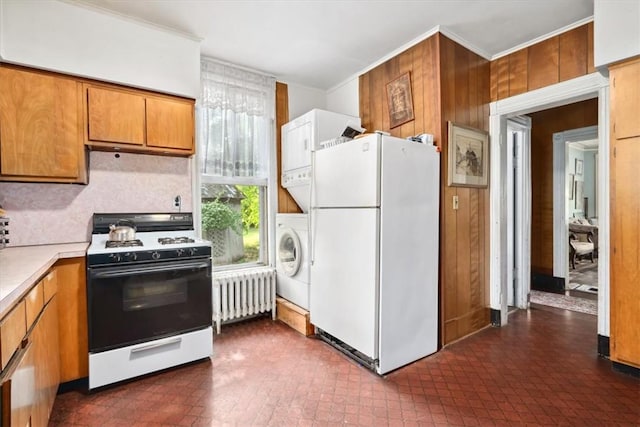 kitchen with wood walls, crown molding, radiator heating unit, white appliances, and stacked washer / dryer