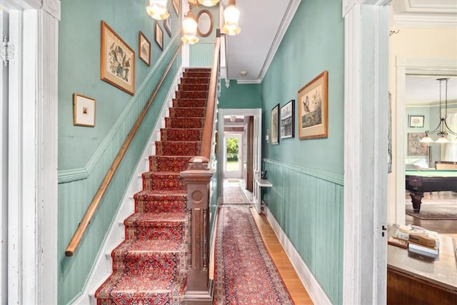 staircase with crown molding, wood-type flooring, and a notable chandelier