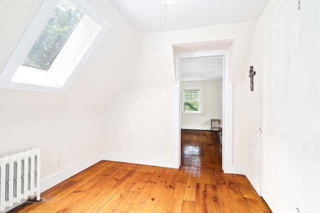 additional living space with hardwood / wood-style flooring, radiator heating unit, and a skylight