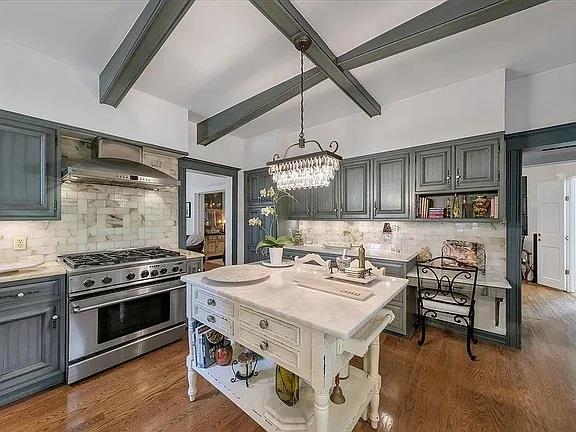 kitchen with pendant lighting, decorative backsplash, high end stove, and an island with sink