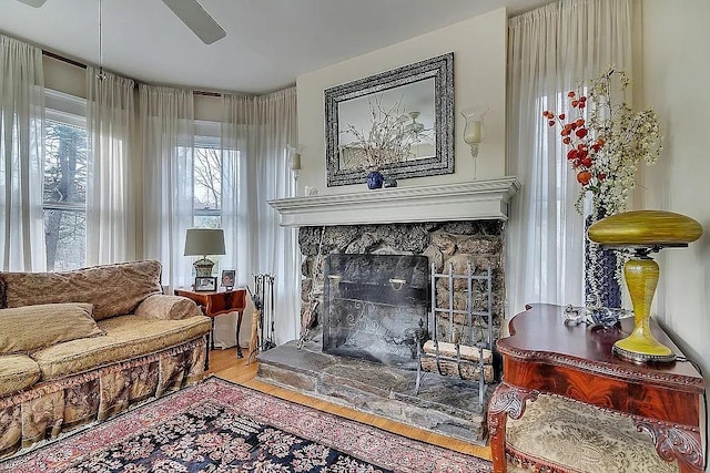 sitting room with hardwood / wood-style floors, a stone fireplace, and ceiling fan