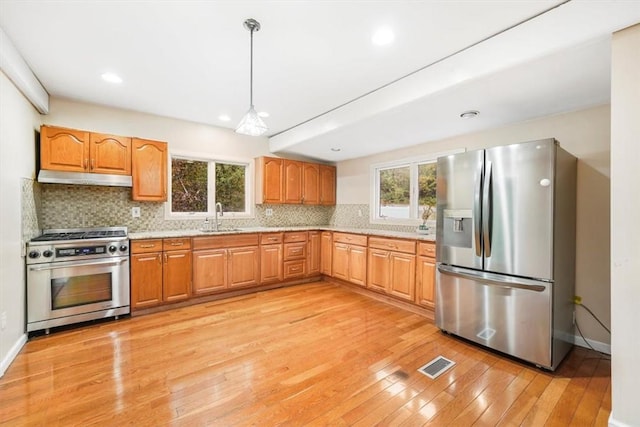 kitchen with appliances with stainless steel finishes, light wood-type flooring, tasteful backsplash, and plenty of natural light