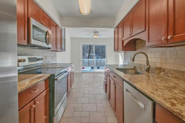 kitchen with light stone counters, sink, stainless steel appliances, and ceiling fan