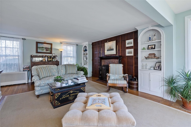 living room with radiator, built in features, a fireplace, and light hardwood / wood-style flooring