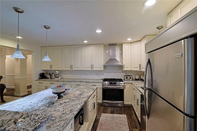 kitchen featuring dark wood-type flooring, hanging light fixtures, wall chimney exhaust hood, light stone countertops, and appliances with stainless steel finishes