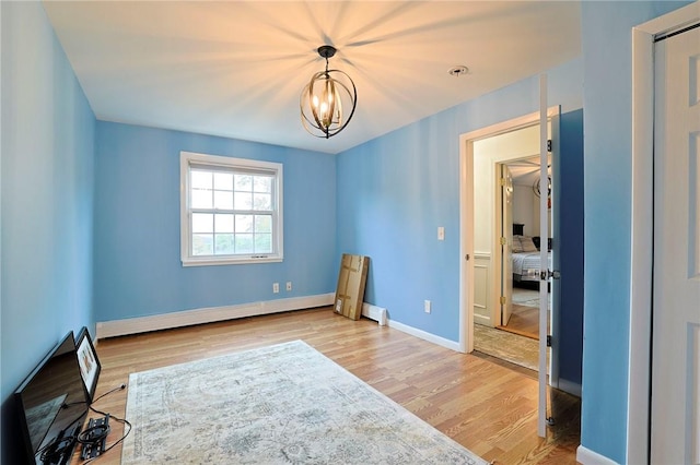 empty room with light hardwood / wood-style floors, a baseboard heating unit, and an inviting chandelier