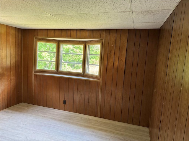 empty room with wood walls, hardwood / wood-style floors, and a drop ceiling