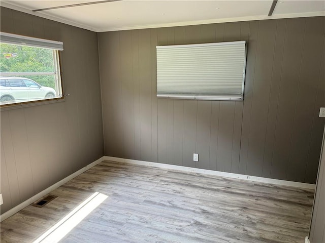 spare room featuring ornamental molding, light hardwood / wood-style floors, and wooden walls