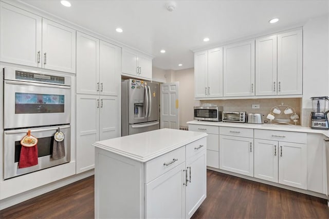 kitchen with tasteful backsplash, white cabinets, dark wood-type flooring, and appliances with stainless steel finishes