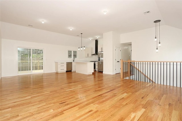 unfurnished living room featuring light wood-type flooring, sink, and high vaulted ceiling