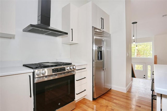 kitchen with appliances with stainless steel finishes, wall chimney exhaust hood, light hardwood / wood-style flooring, white cabinets, and hanging light fixtures