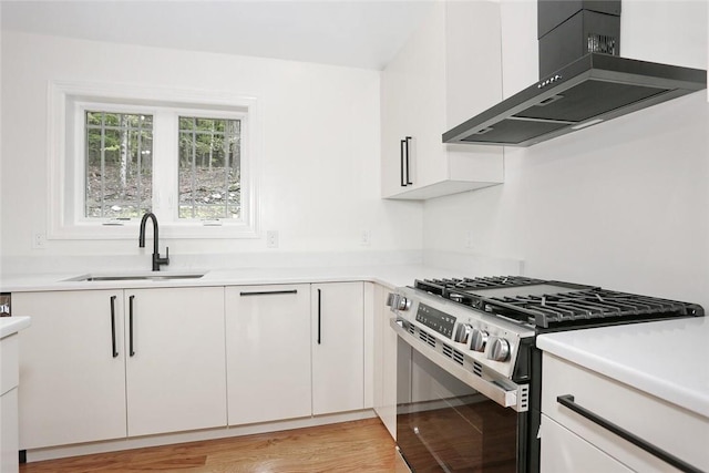 kitchen featuring wall chimney range hood, sink, white cabinets, and stainless steel gas range