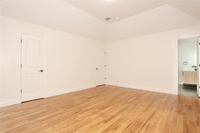 empty room with light hardwood / wood-style floors and vaulted ceiling