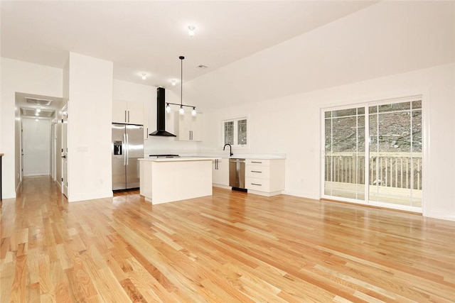 kitchen with light wood-type flooring, wall chimney exhaust hood, stainless steel appliances, decorative light fixtures, and white cabinets