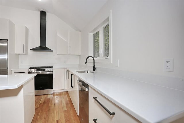 kitchen featuring white cabinets, light wood-type flooring, wall chimney range hood, and appliances with stainless steel finishes